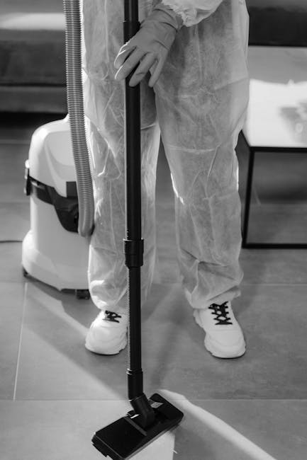 A professional cleaner from Carpet Cleaning Lambeth dressed in a white protective suit, gloves, face mask, and shoe covers, using a steam cleaning machine to deep clean a beige carpet in a bright livi